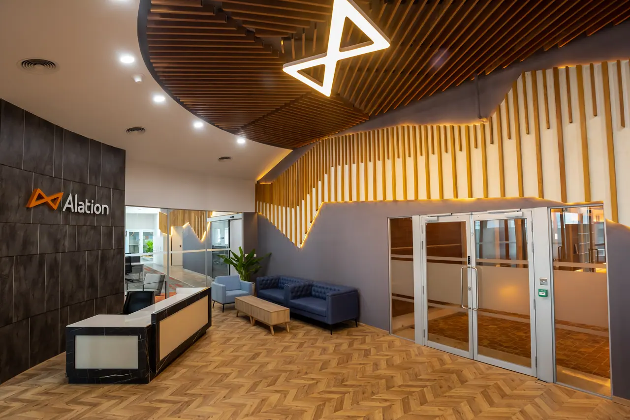Reception with an Alation logo wall, marble-edged desk, blue tufted sofa, herringbone floor and a lit timber batten wall