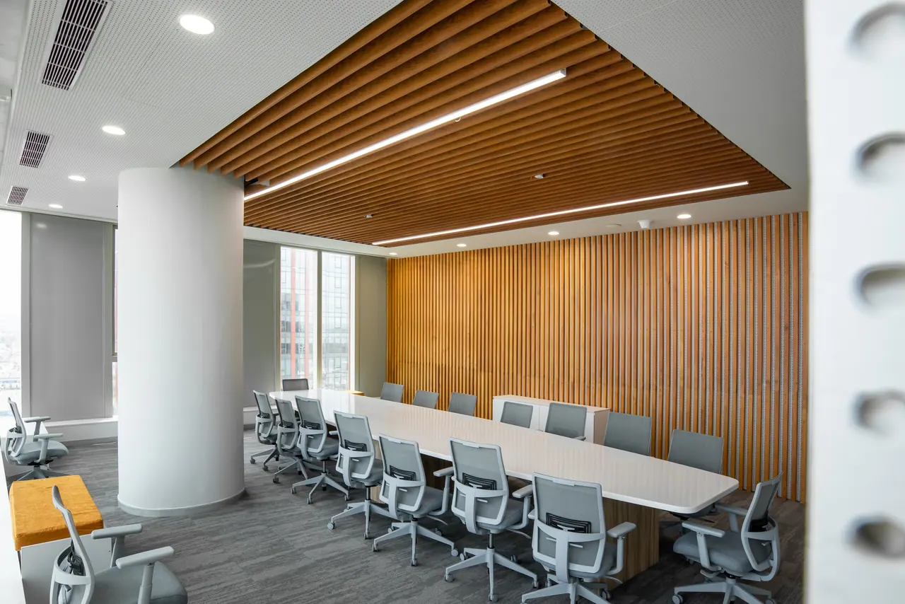 Boardroom with a long white table, grey mesh chairs, a wood baffle ceiling with linear lights and a timber slat wall
