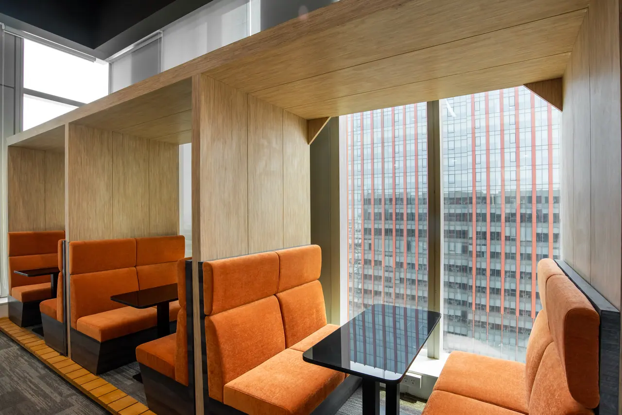Orange upholstered booths in timber-lined bays with black tables, set against a window facing a neighbouring glass tower