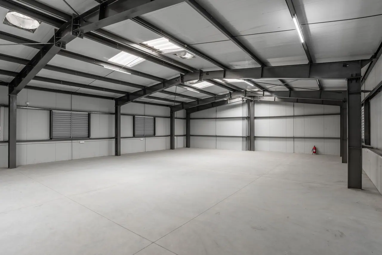 Upper floor with steel portal frames, skylights, louvred vents, white wall panels and a wide grey concrete floor