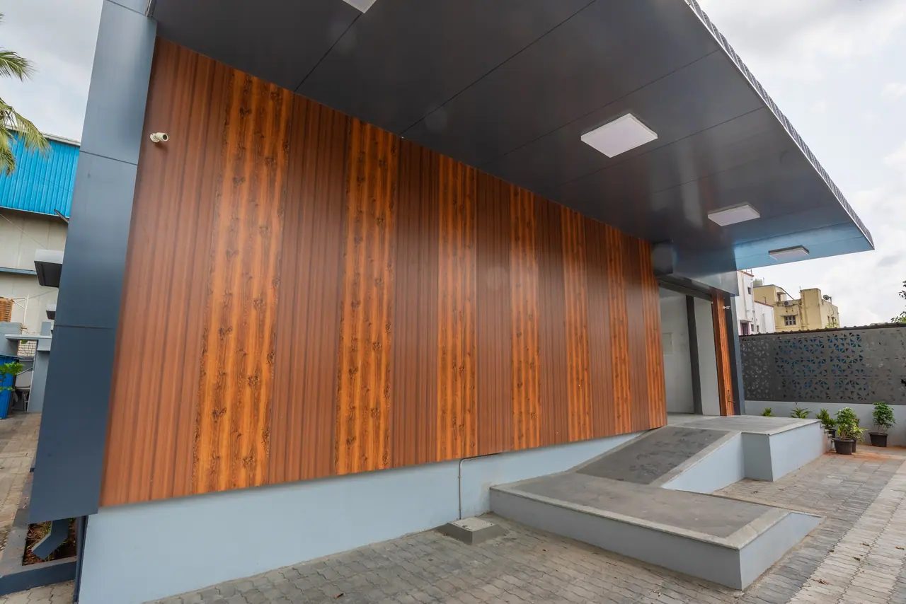 Wood-look cladding under a deep dark canopy with ceiling lights, beside a raised concrete entrance platform and ramp