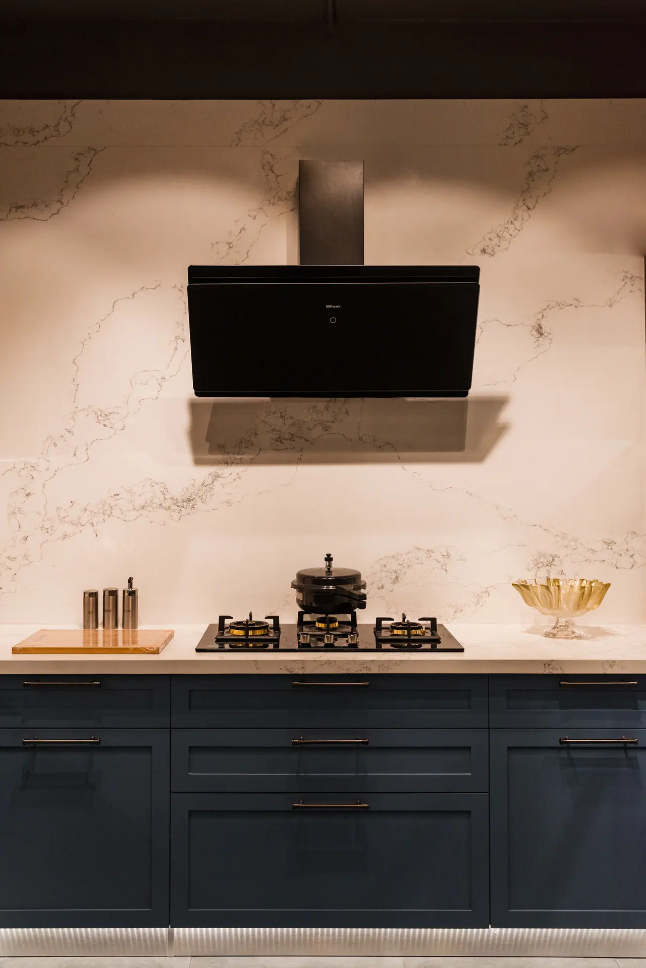 Black angled chimney hood above a gas hob on a white marble-look backsplash, with navy shaker drawers below