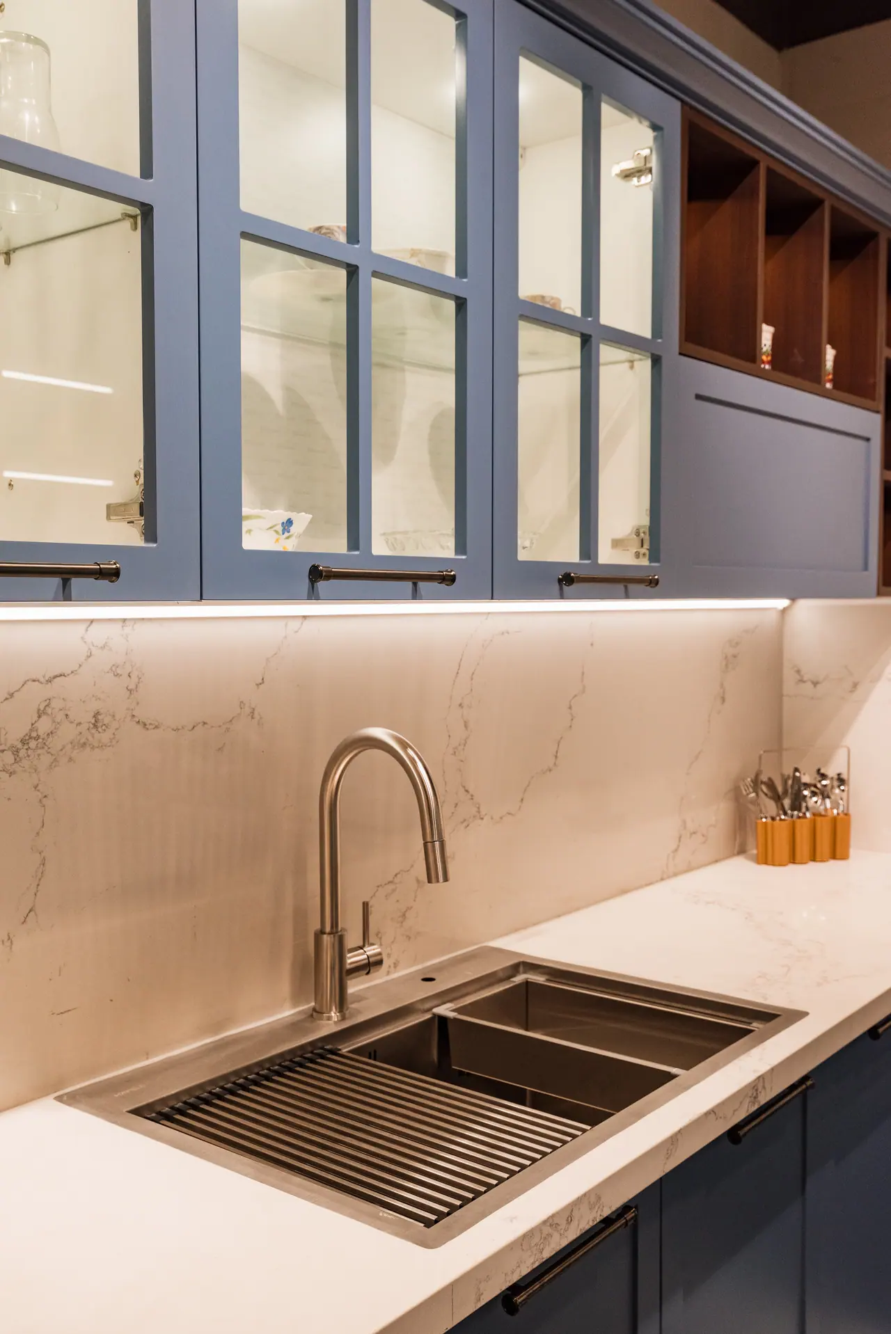 Stainless steel sink with a roll-up drying rack and pull-down tap beneath blue glass-front wall cabinets