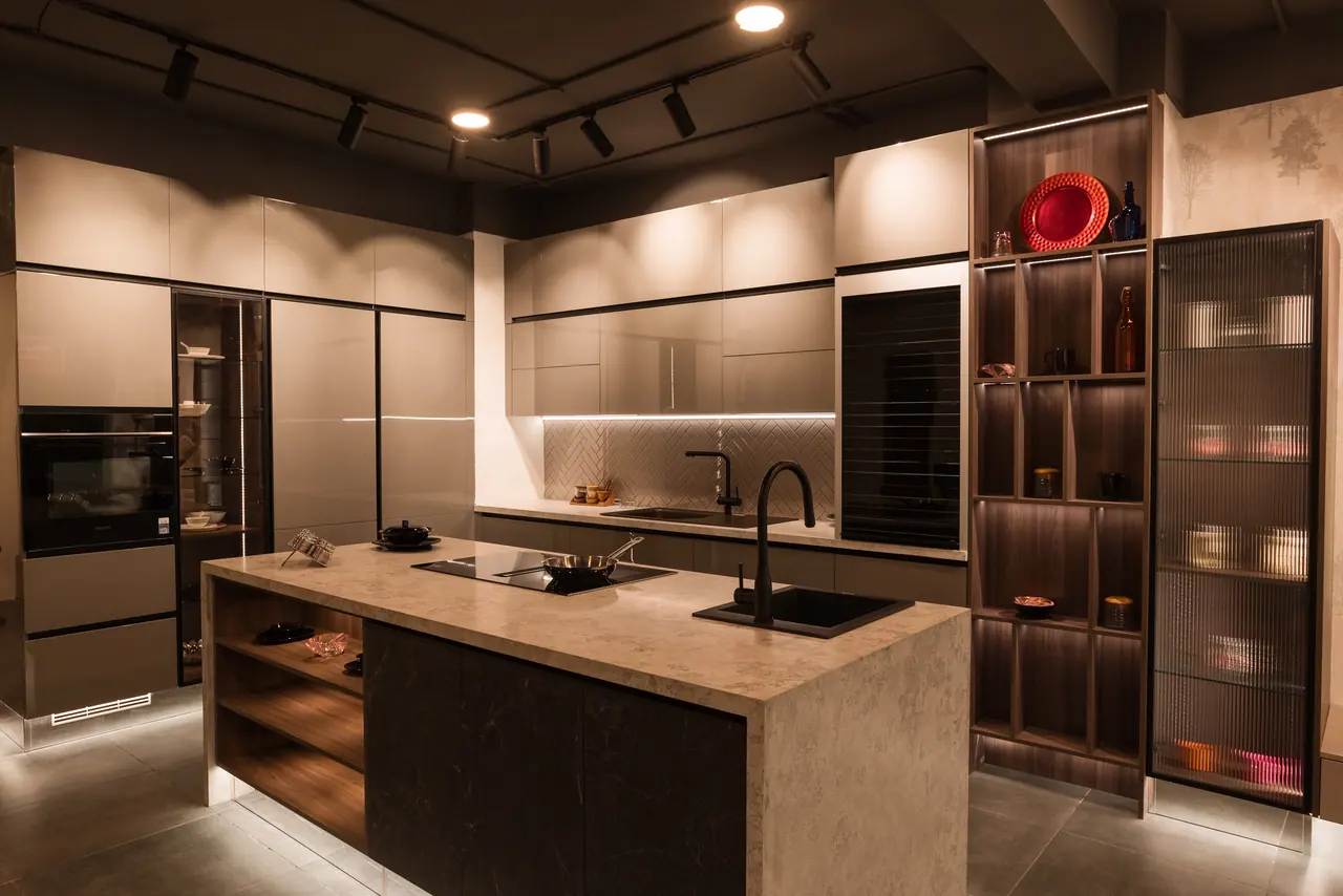 Island kitchen display with a stone-look worktop, induction hob and black sink, champagne gloss cabinets and lit shelving