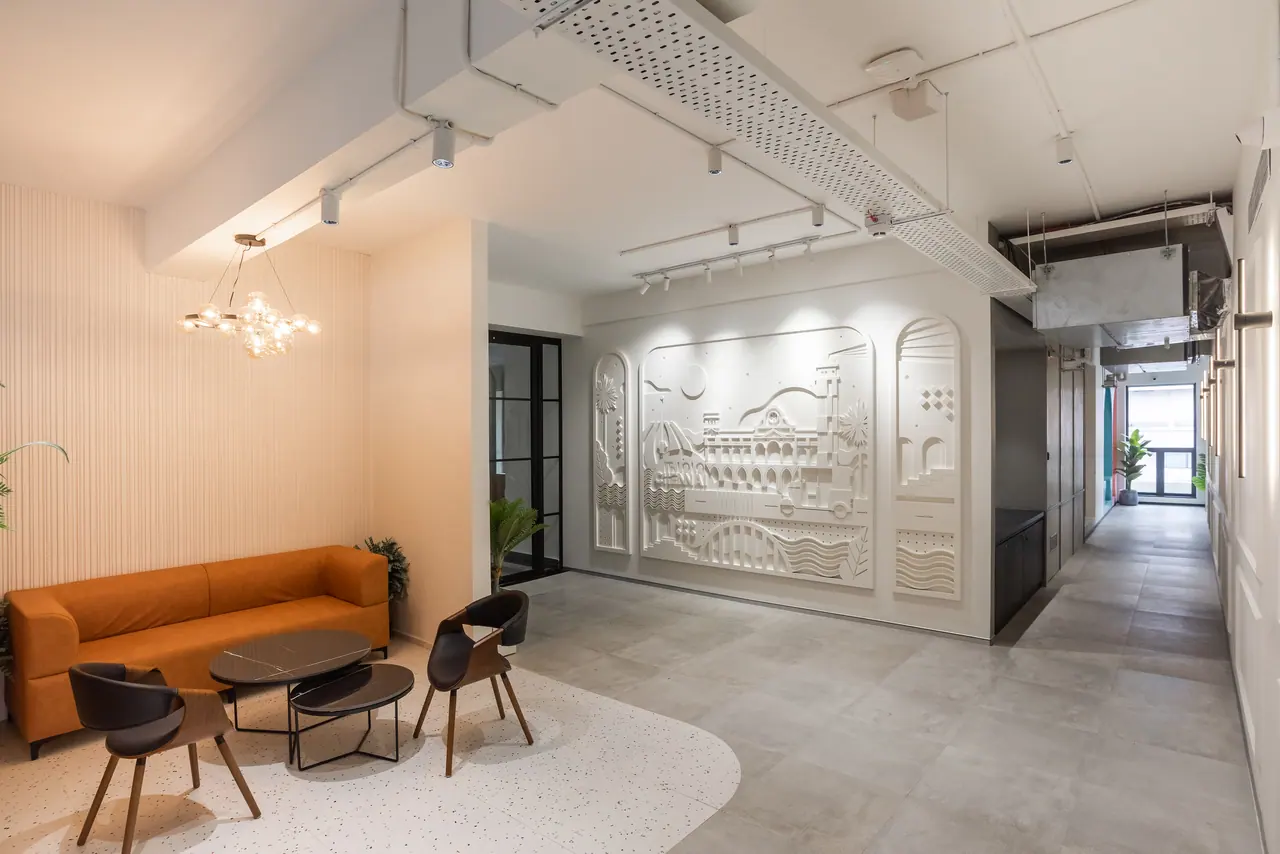 Lounge with an orange sofa, black side chairs and a bubble chandelier beside a white relief mural and a long corridor