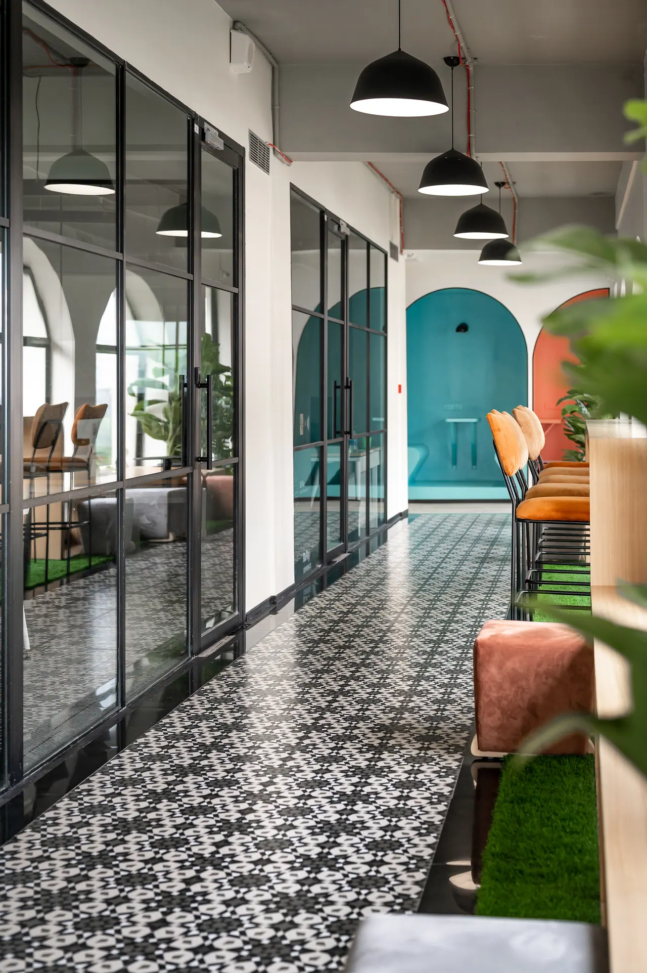 Corridor with black and white patterned tiles, black-framed glass doors and pendants leading to a teal arched niche