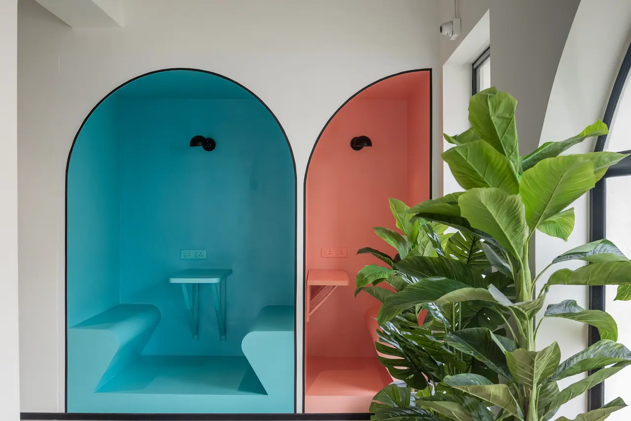 Two arched seating niches painted teal and coral, each with built-in benches, a small table and a black wall lamp