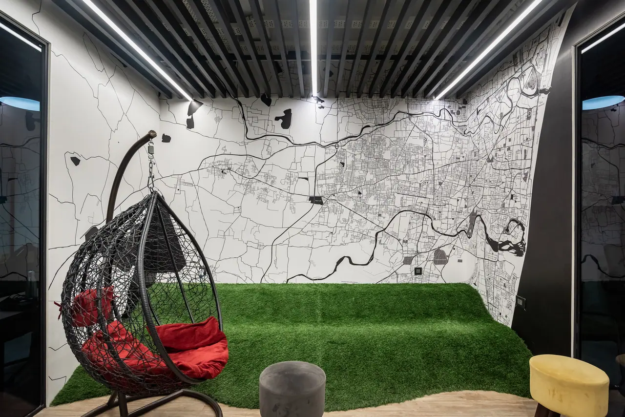 Breakout room with a street-map mural, an artificial turf seating mound, a hanging rattan egg chair and a slatted ceiling
