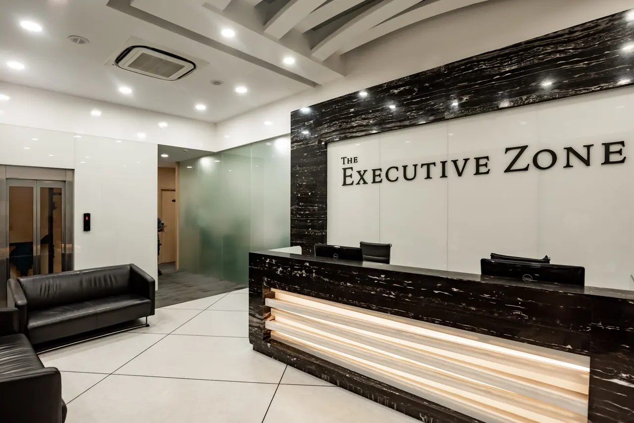 Reception with a black marble-clad desk over lit timber slats, The Executive Zone lettering, leather sofas and a lift
