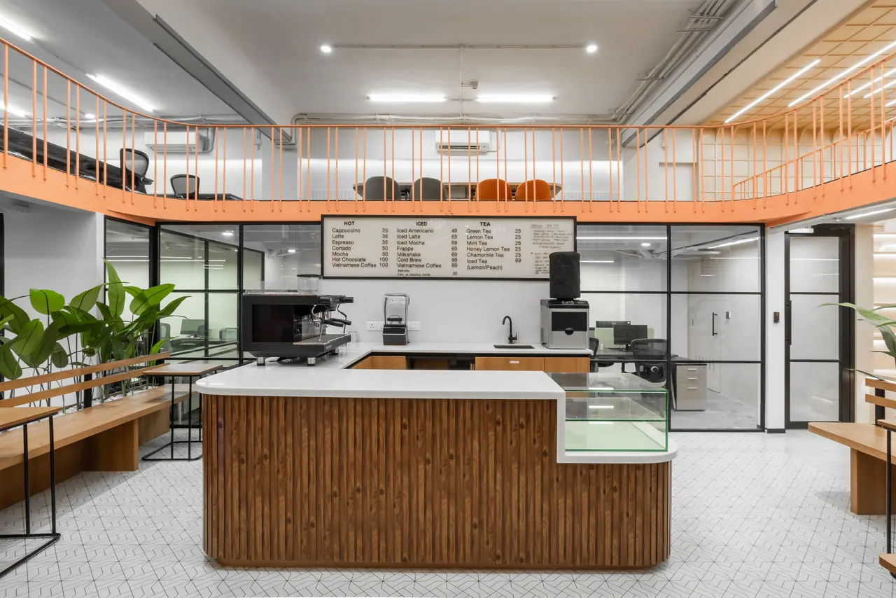 Café counter with a fluted timber front, espresso machine and menu board beneath an orange-railed mezzanine