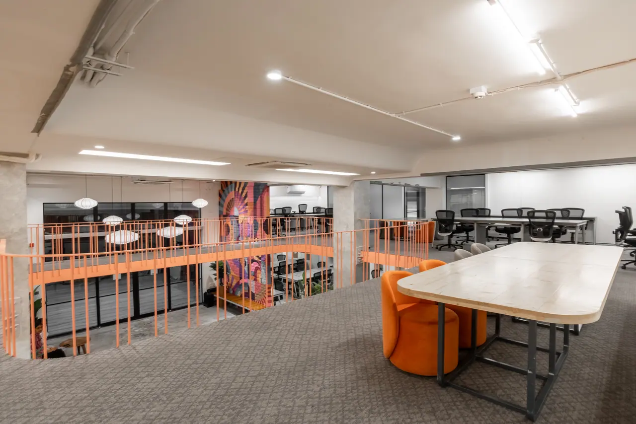 Mezzanine workspace with an orange railing overlooking the floor below, a long timber table and orange velvet chairs