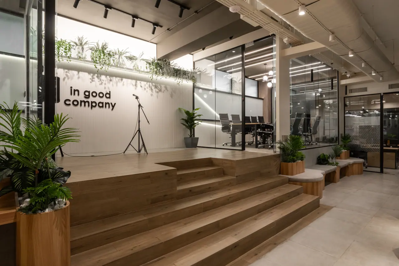 Raised timber stage with steps, a microphone stand and in good company lettering on a fluted wall under hanging plants