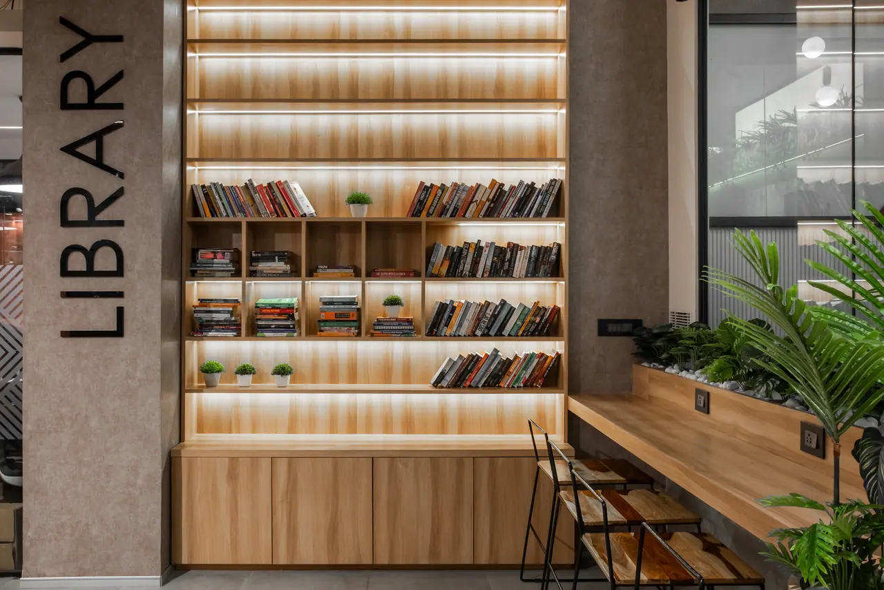 Library nook with backlit timber shelves of books, LIBRARY lettering on a textured pillar and a counter with stools