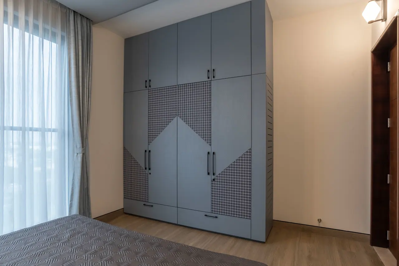 Tall blue-grey wardrobe with houndstooth fabric inlays in a chevron pattern, slim black handles and a louvred side panel