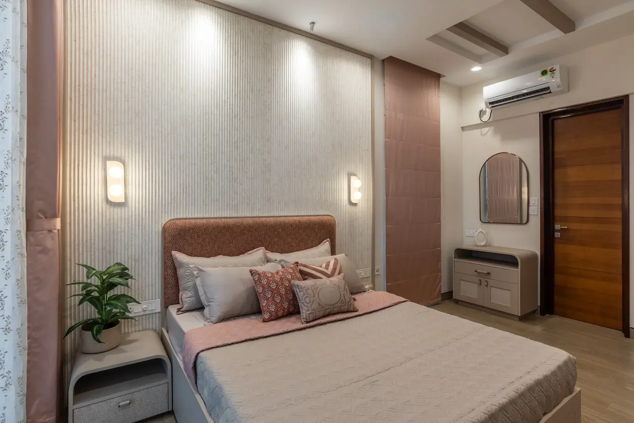 Bedroom with a rust upholstered headboard against a fluted panel wall, twin wall lights, a blush blind and a dresser