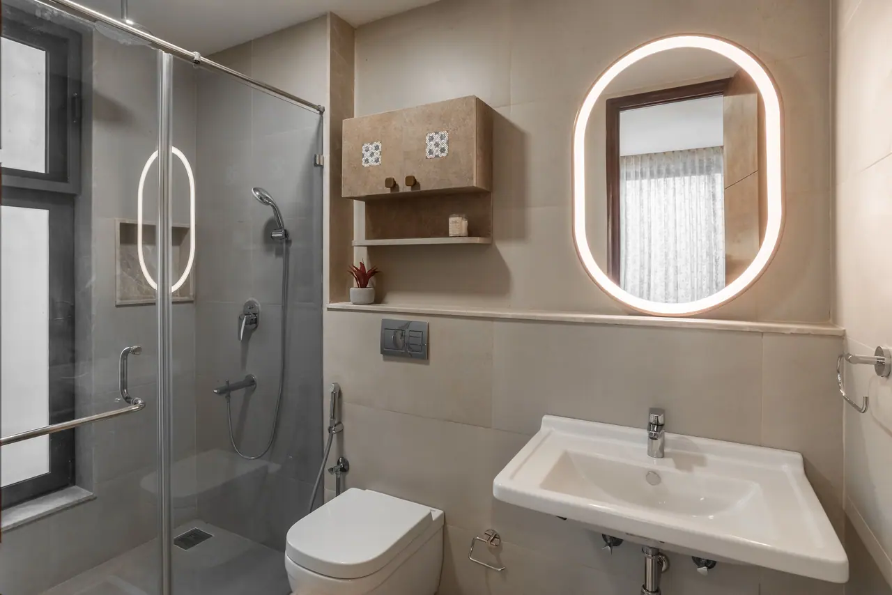 Bathroom with a backlit oval mirror, beige stone tiles, a wall-hung WC, a glass shower enclosure and a small cabinet