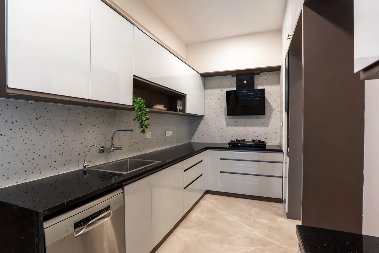White handleless kitchen with a black granite counter, terrazzo-look backsplash, open shelf, black hood and dishwasher