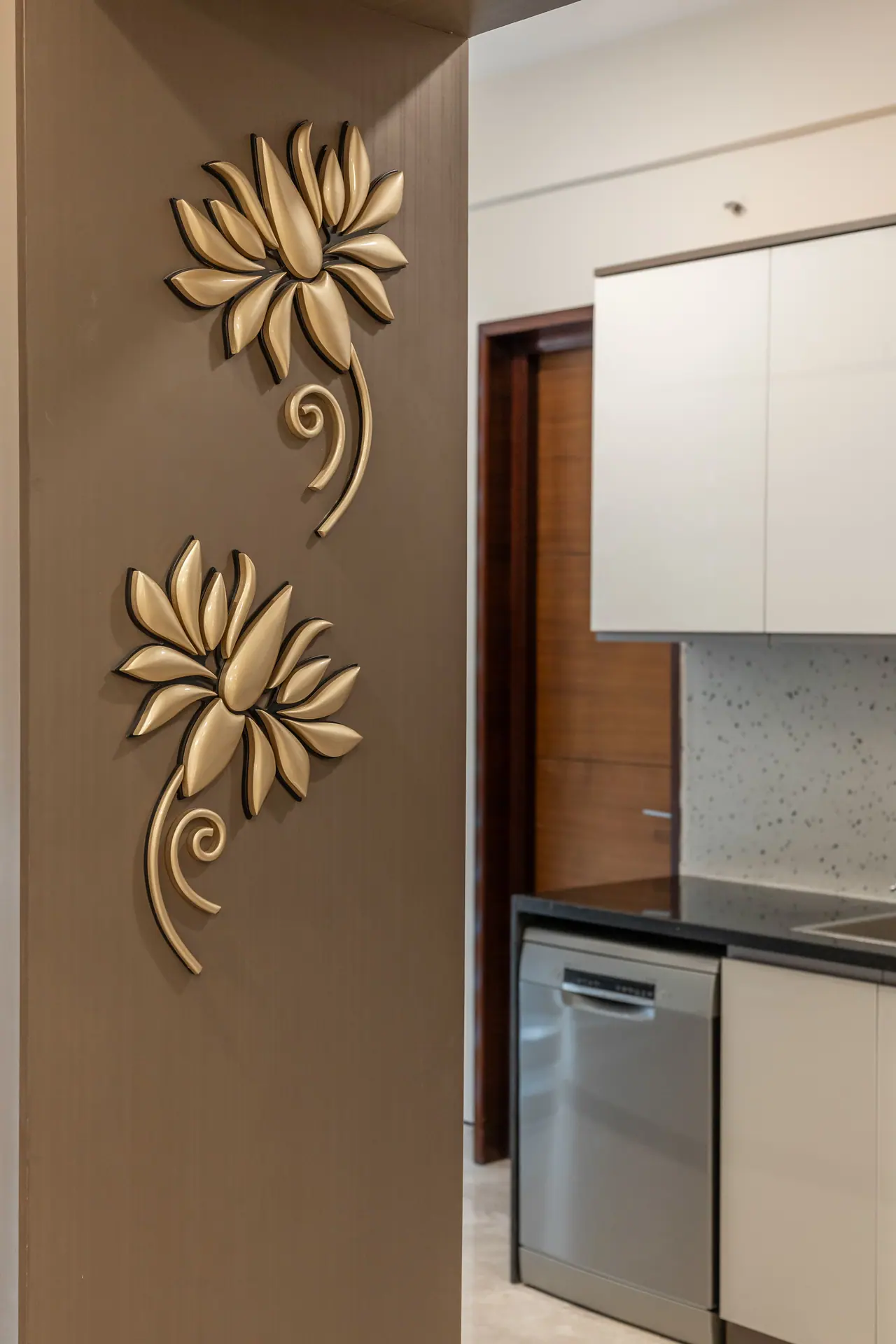 Two gold lotus motifs on a taupe wall panel beside the kitchen, with white cabinets and a dishwasher beyond