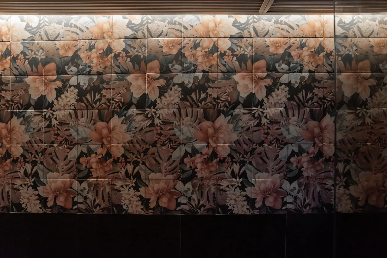 Wall of large floral tiles in peach, rust and grey, lit from above by a concealed strip, with a dark stone band below