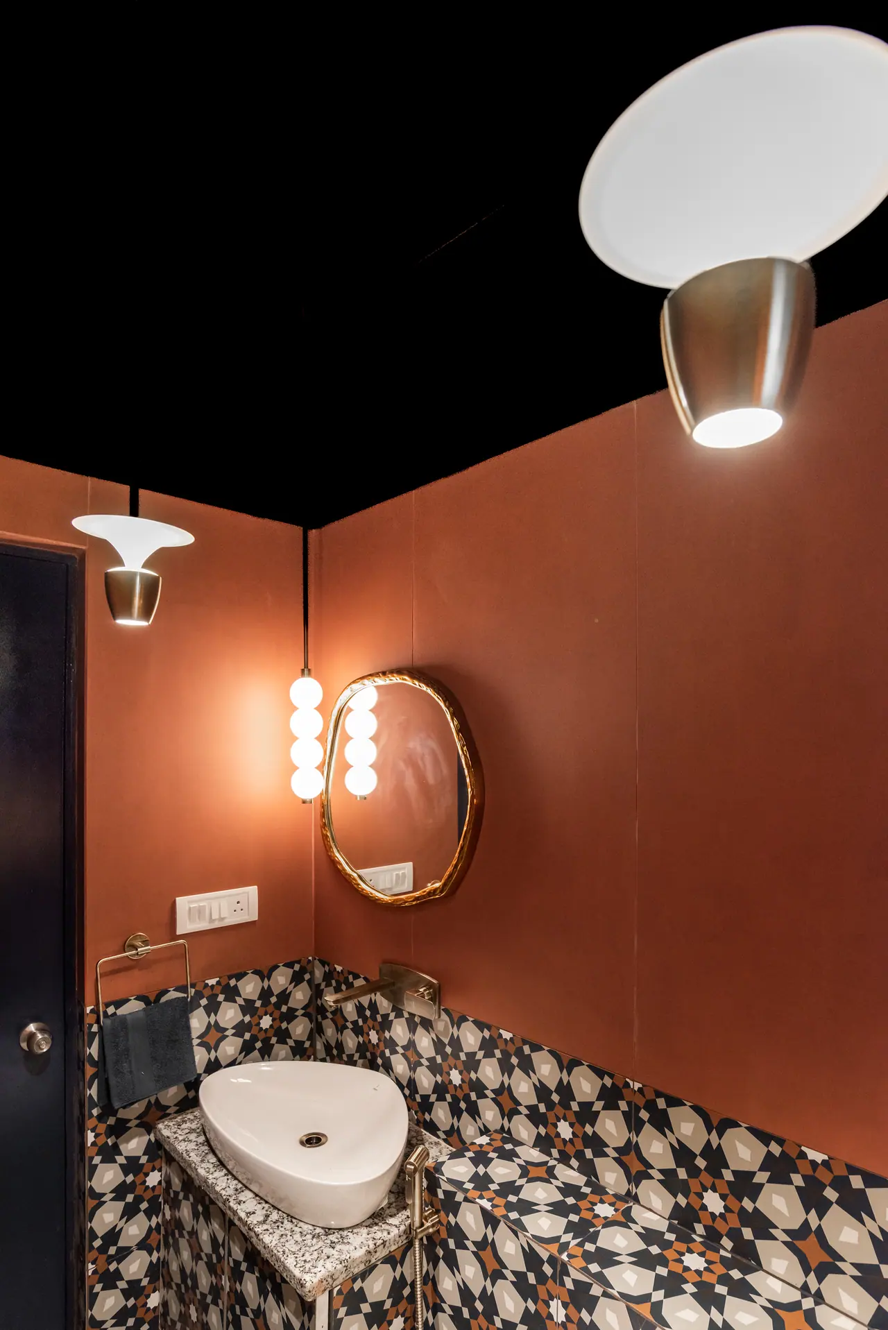 Powder room with terracotta walls, a black ceiling, star-pattern tiles, a vessel basin, a gold-framed mirror and globe light