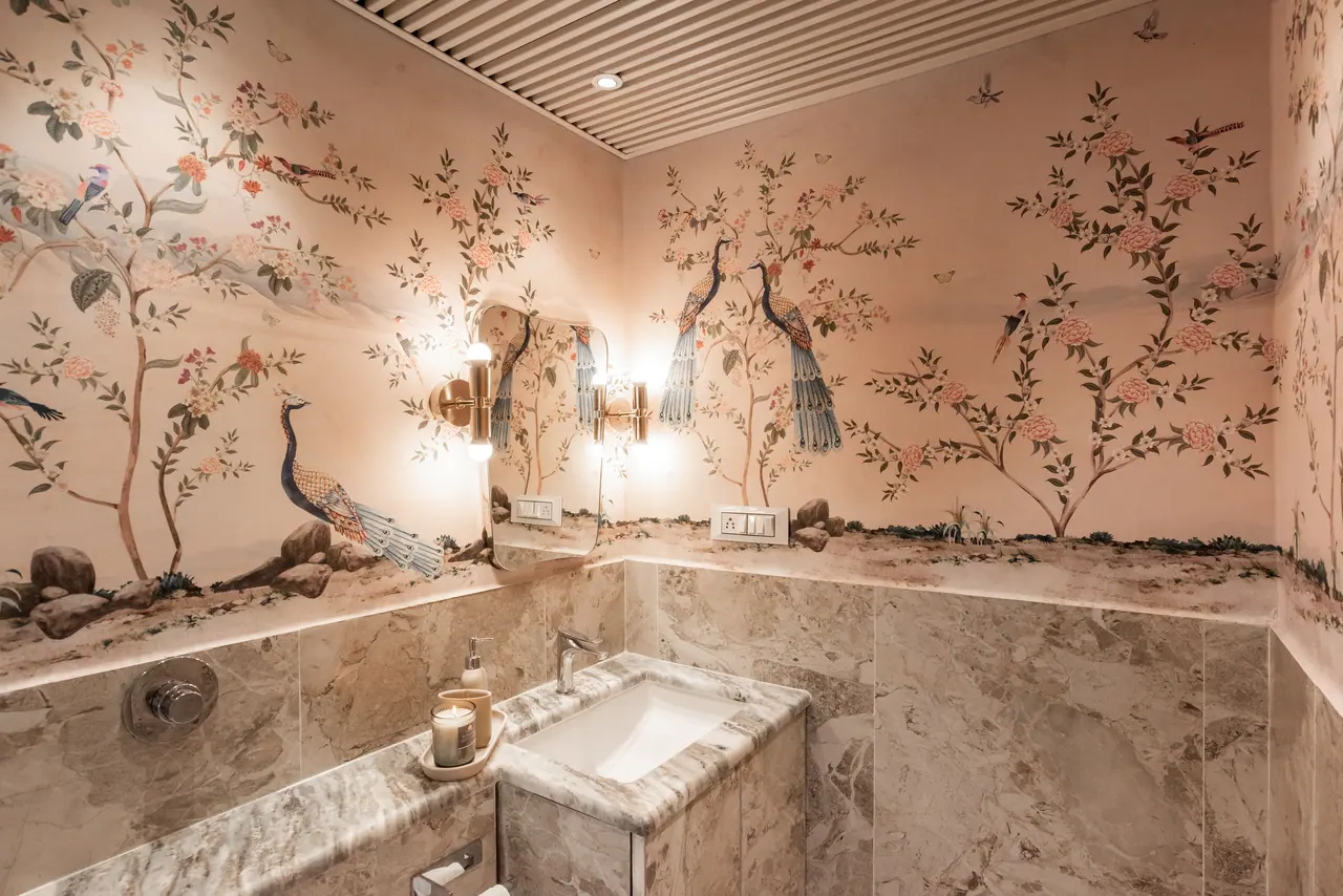 Powder room with a peacock and blossom-tree wall print above grey marble cladding, an undermount basin and brass sconces