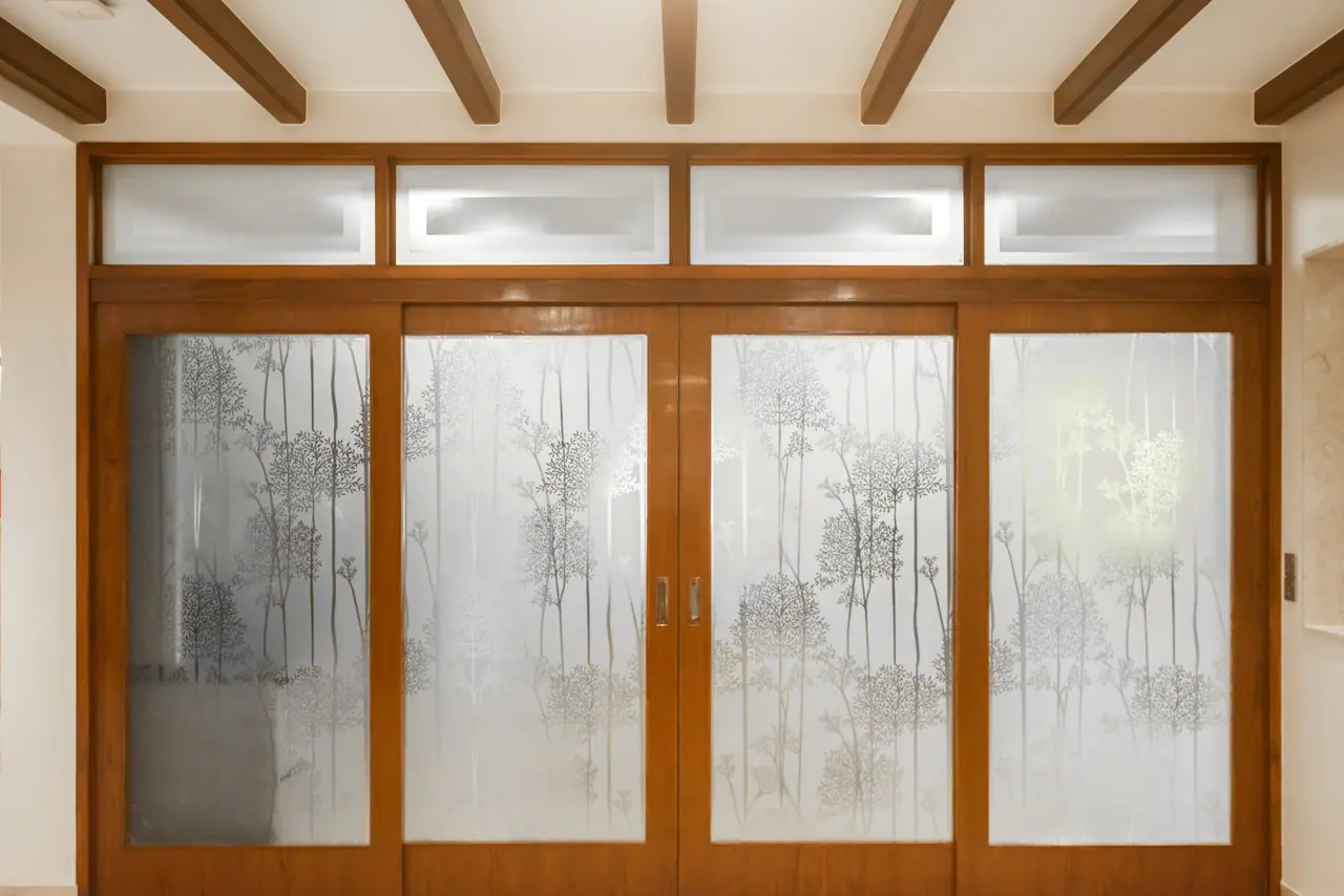 Wood-framed sliding doors with frosted tree-pattern glass panels and clerestory lights beneath exposed ceiling beams