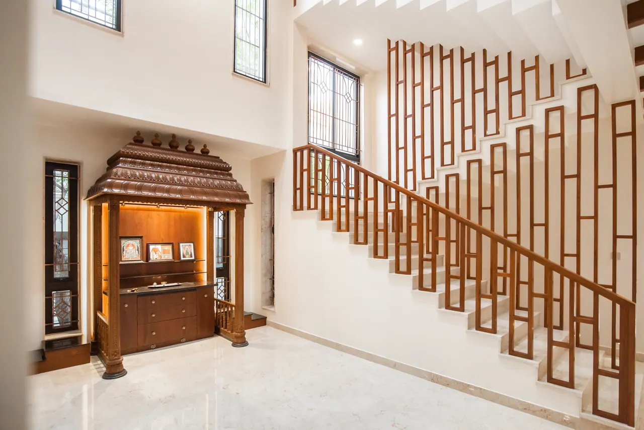 Hall with a carved wooden prayer unit beside a stone-tread staircase with a timber handrail and a tall timber grid screen