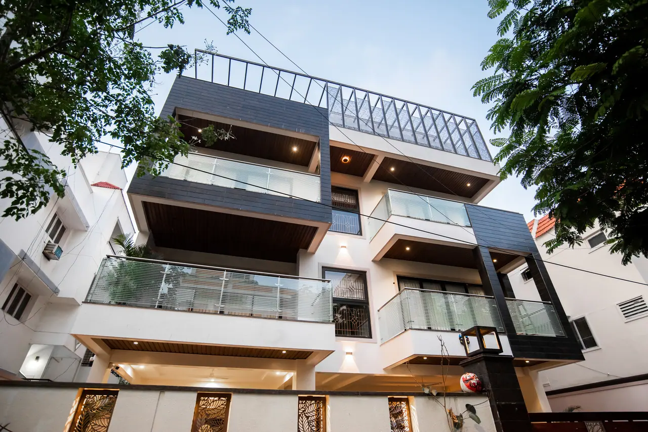 Multi-storey house facade with dark tiled frames, glass balcony railings, wood-lined soffits and leaf-cut boundary panels