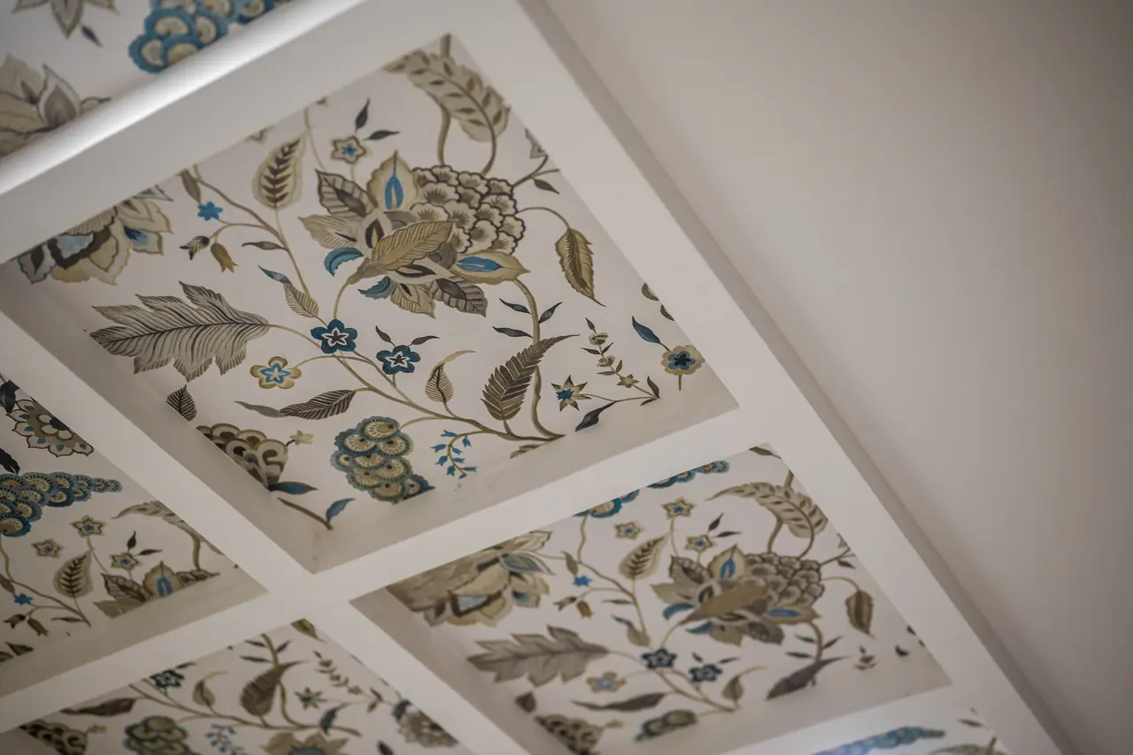 Close view of coffered ceiling panels printed with large floral and leaf motifs in olive, cream and blue within white frames