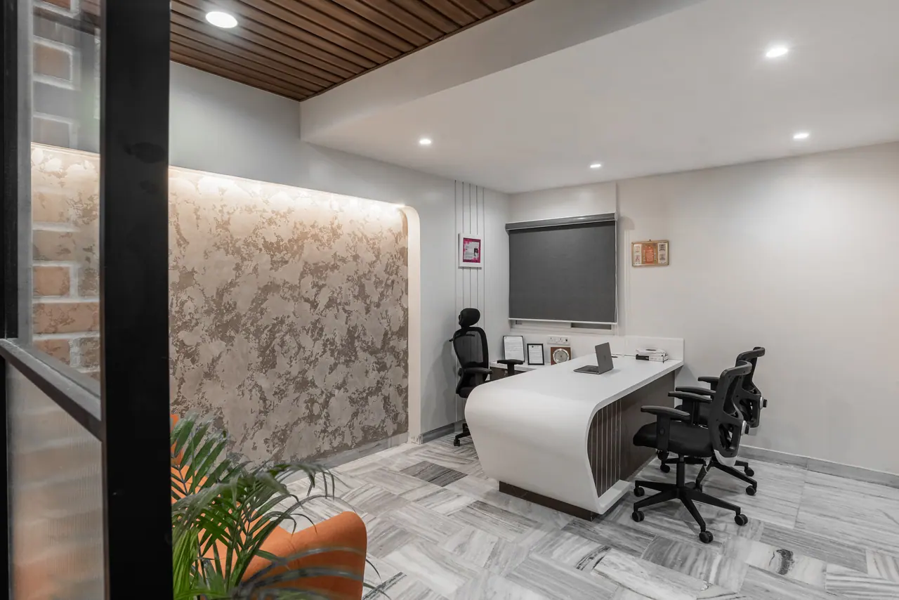 Cabin with a curved white desk, mesh chairs, roller blind and a backlit textured feature wall under a wood-slat ceiling