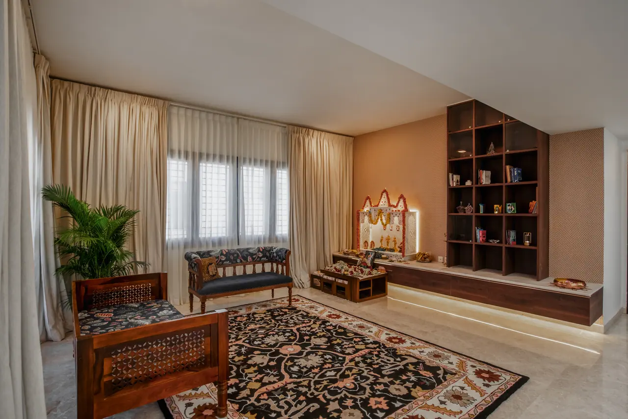 Sitting room with a lattice-sided wooden daybed, upholstered settee, dark floral rug, lit prayer unit and walnut shelving
