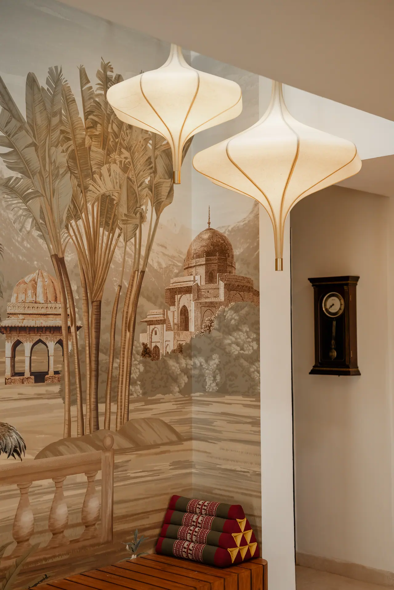 Sepia landscape mural with palms and domed pavilions beside two sculptural fabric pendants and a wall-mounted pendulum clock