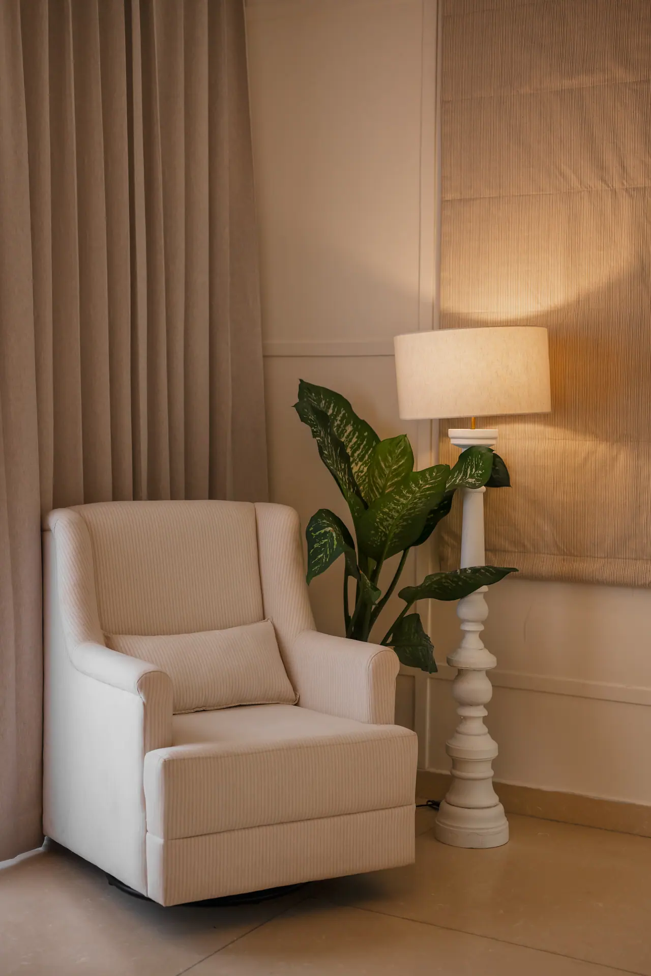 Cream wingback armchair beside a turned white floor lamp and a leafy plant, against a panelled wall and linen curtains