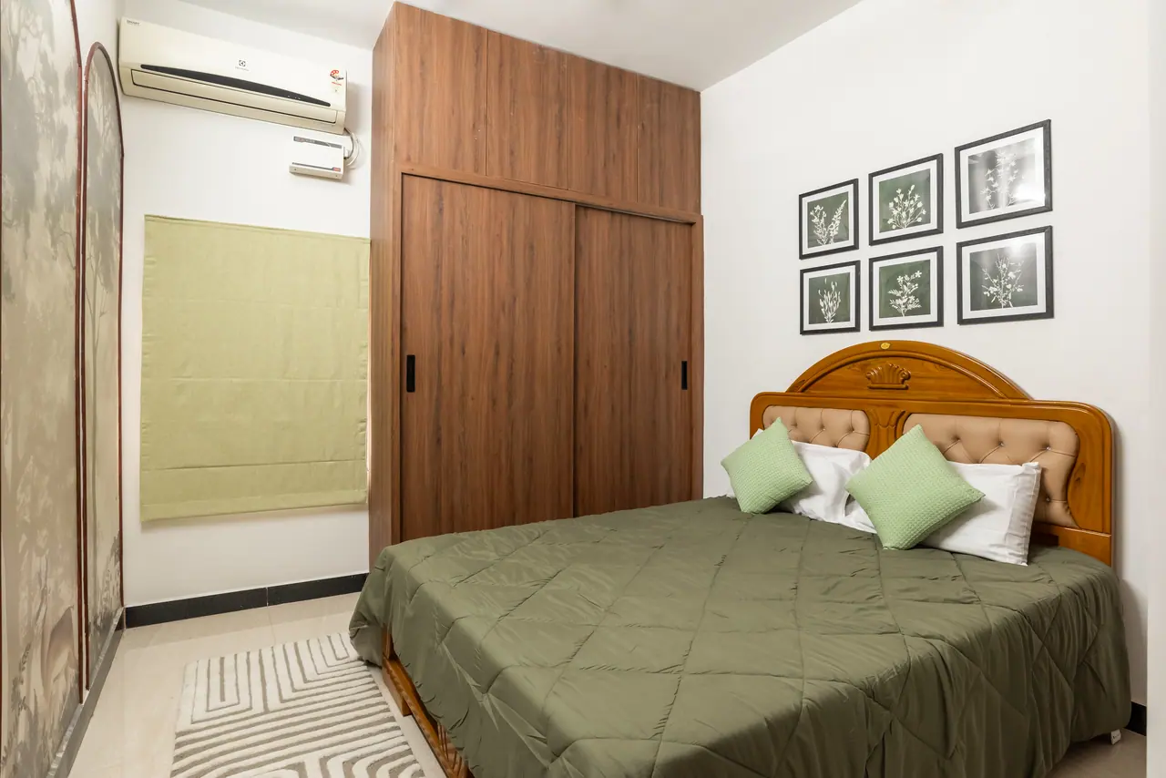 Bedroom with a carved wooden headboard, olive quilted bedspread, sliding wood wardrobe and six framed botanical prints