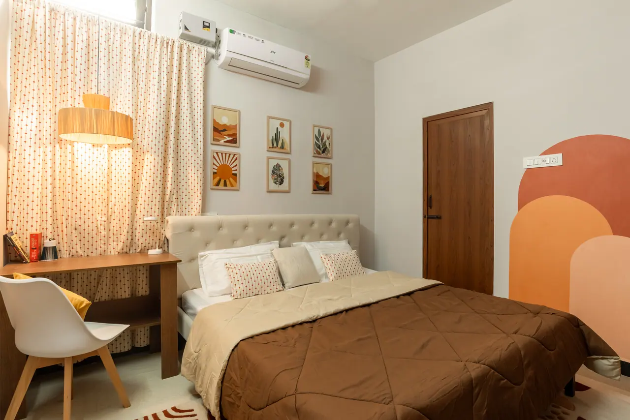 Bedroom with a tufted cream headboard, brown quilt, dotted curtains, fibre drum pendant, study desk and a painted arch motif