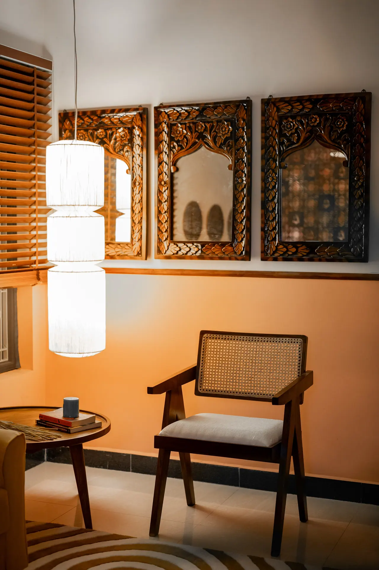 Three carved wooden arched mirrors above a peach dado wall, with a tiered fabric pendant, cane-back armchair and side table