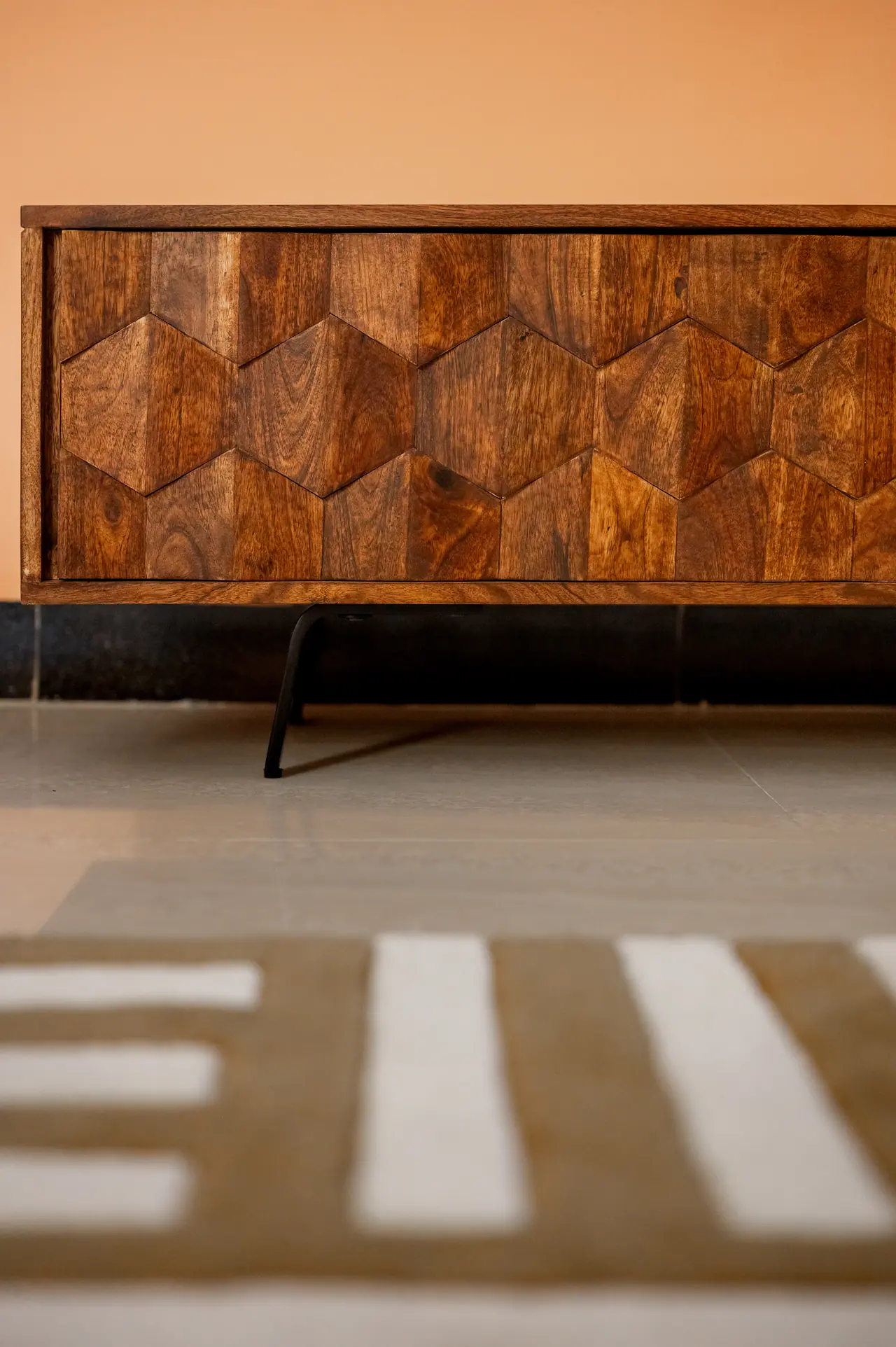 Close view of a wooden sideboard with a hexagon-pattern front on black metal legs, set against a peach wall