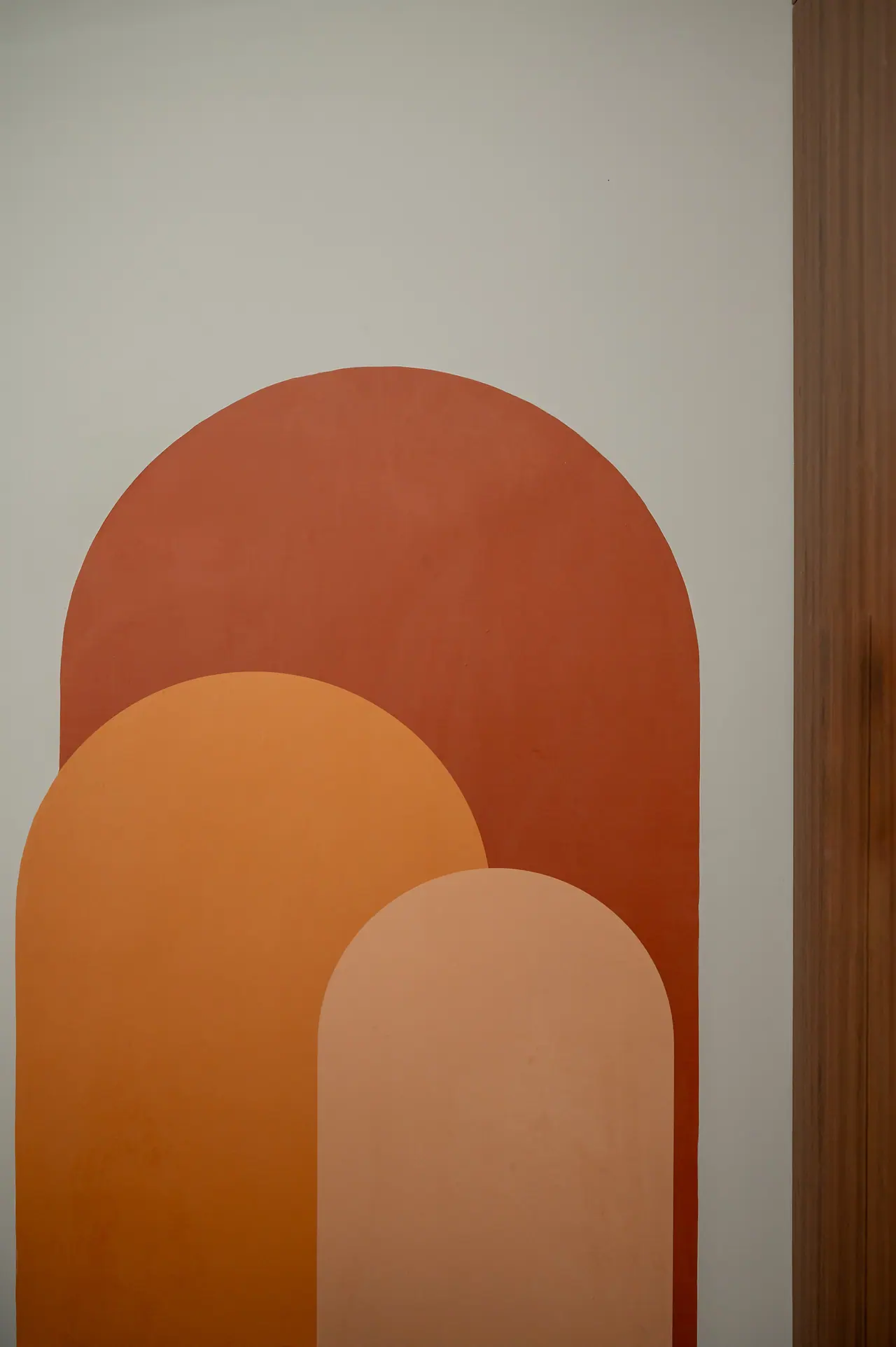Painted overlapping arches in terracotta, orange and blush on a pale grey wall beside a wooden door frame
