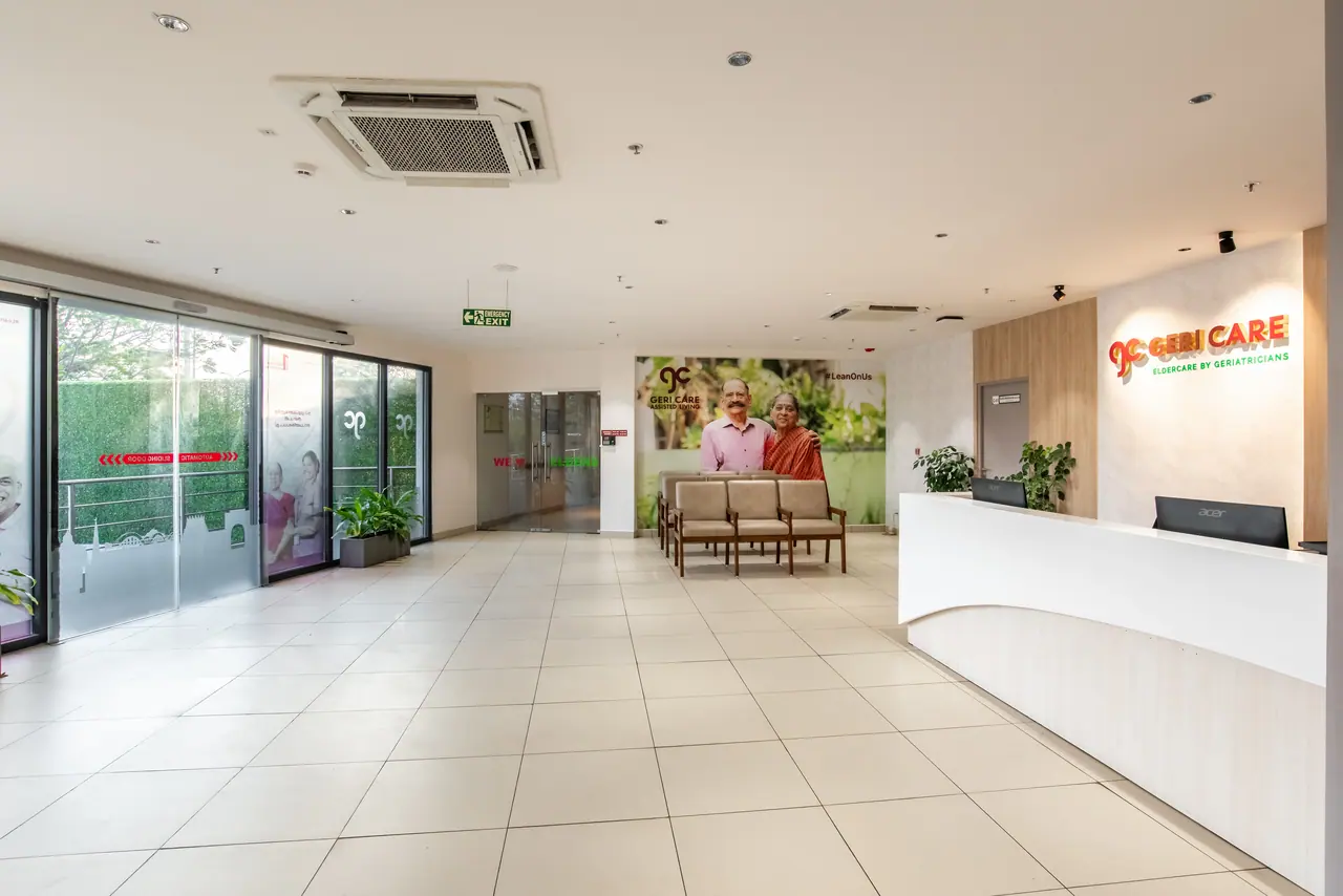 Reception lobby with a curved white desk, Geri Care sign on a pale textured wall, beige waiting chairs and glass entry doors