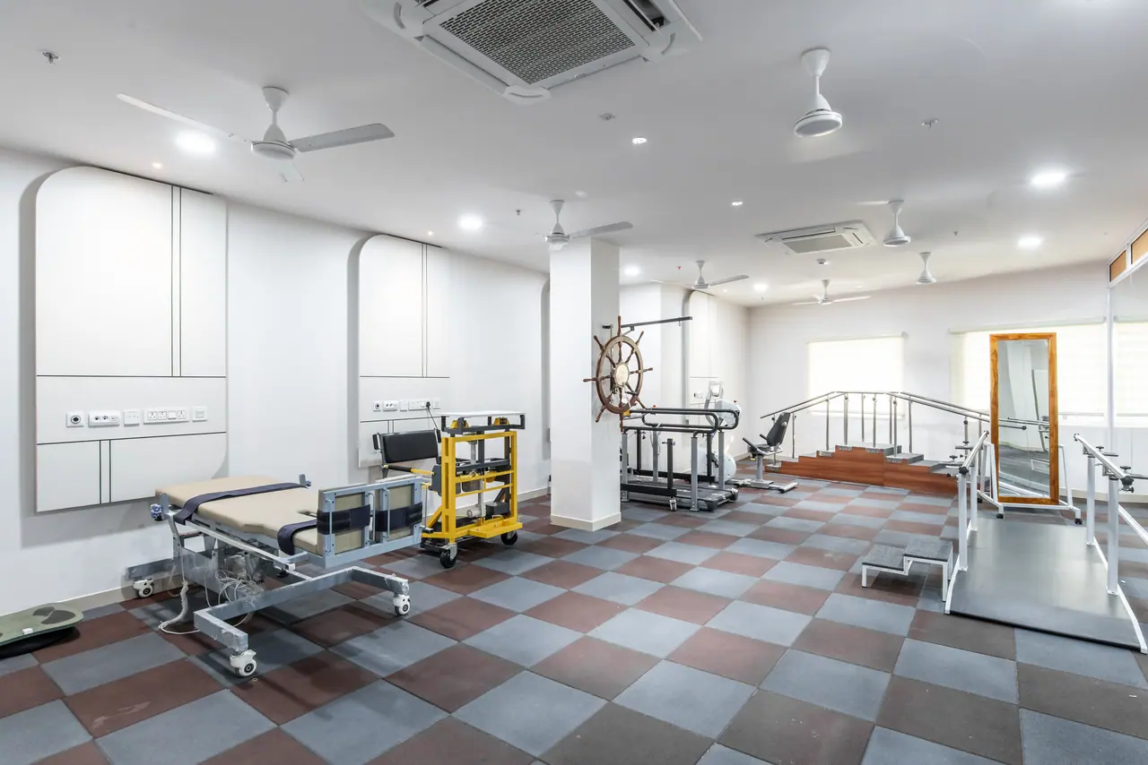 Physiotherapy room with checkerboard rubber floor, treatment table, parallel bars, practice steps, shoulder wheel and mirror