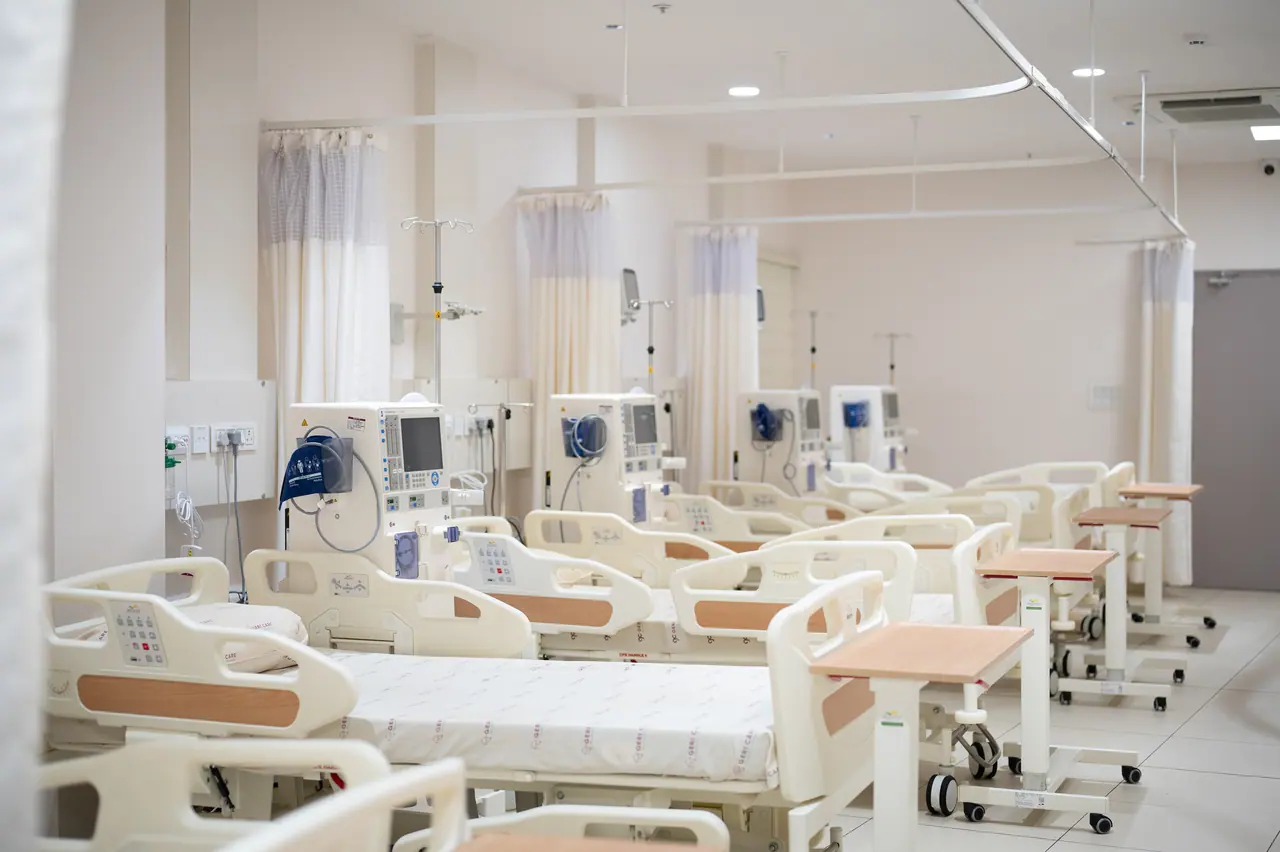 Multi-bed ward with rows of hospital beds, bedside medical machines, overbed tables and privacy curtains on ceiling tracks