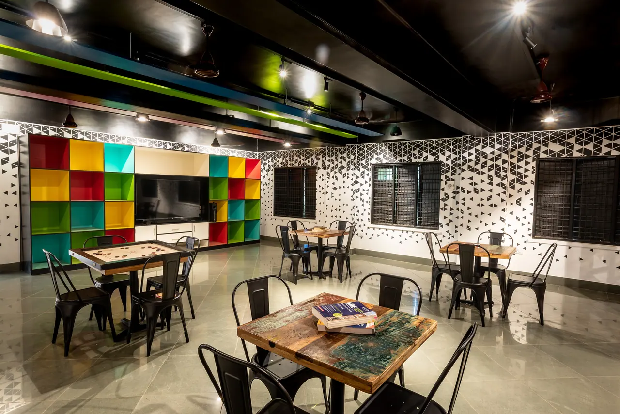 Lounge with a multicoloured cubby shelving wall around a TV, black metal chairs, distressed wood tables and triangle graphics