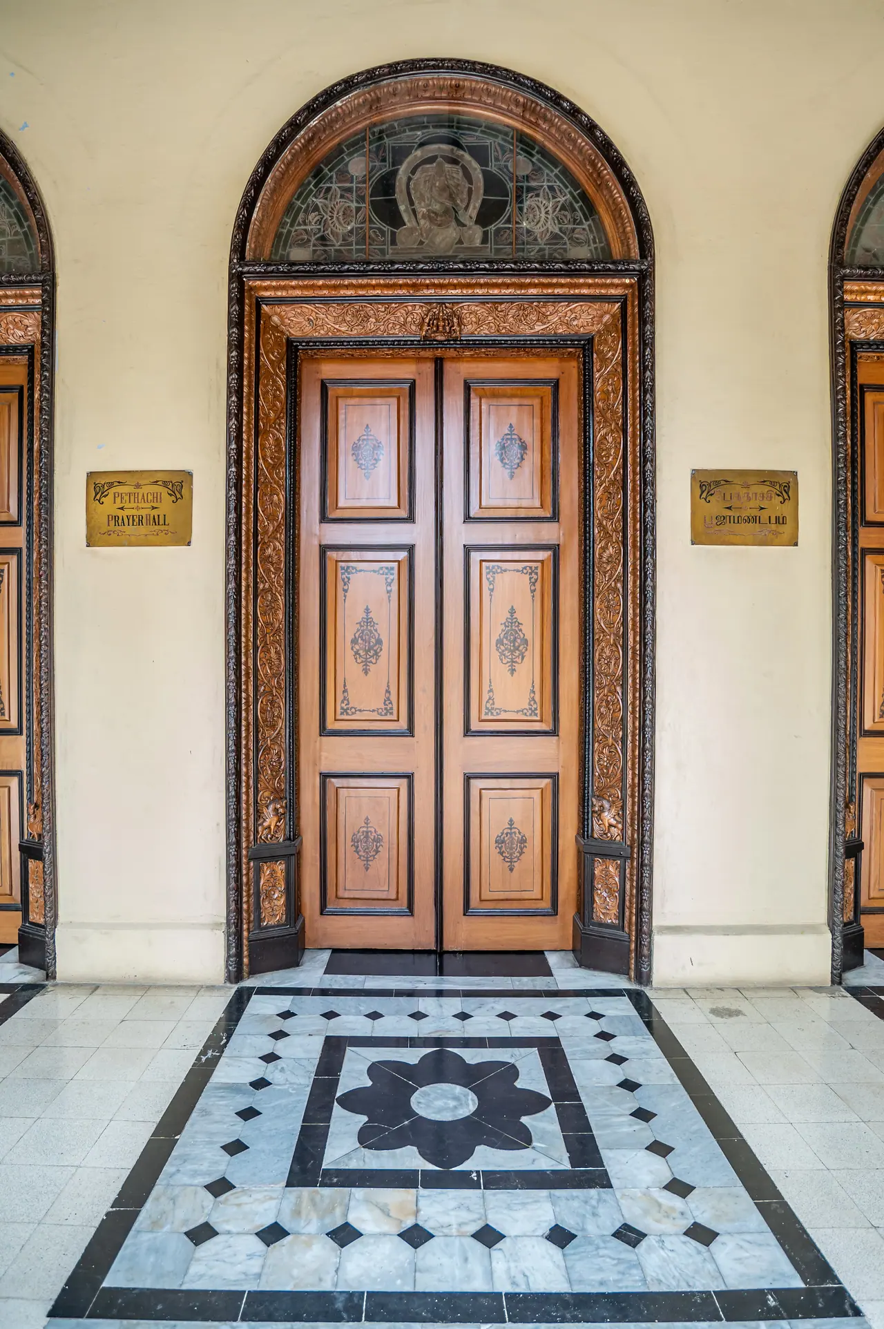 Carved wooden double door under a stained-glass fanlight, with brass plaques and a black and white marble inlay floor