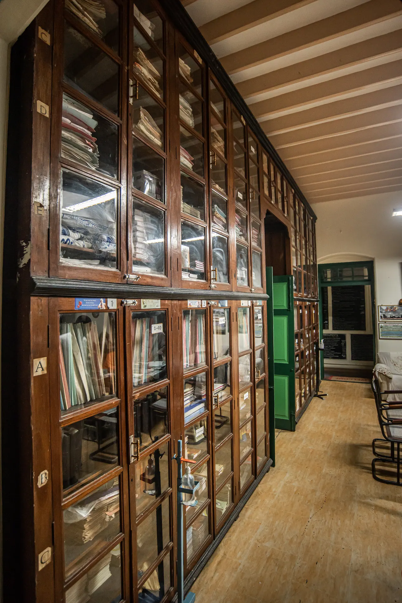 Wall of glass-fronted wooden cabinets holding files and books beside a green door under a beamed ceiling