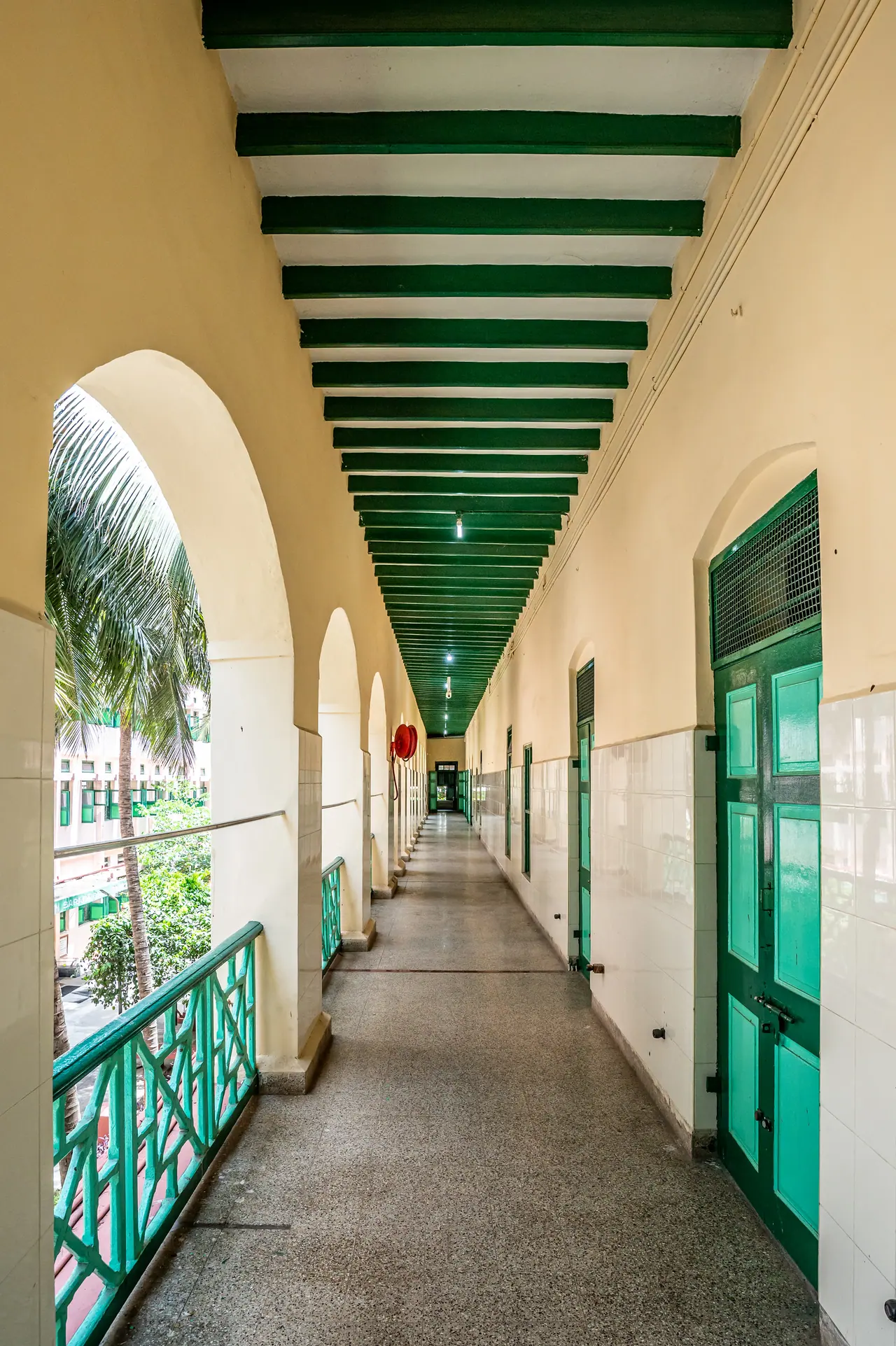 Upper verandah corridor with green ceiling beams, arched openings, green railings and tiled walls in soft daylight