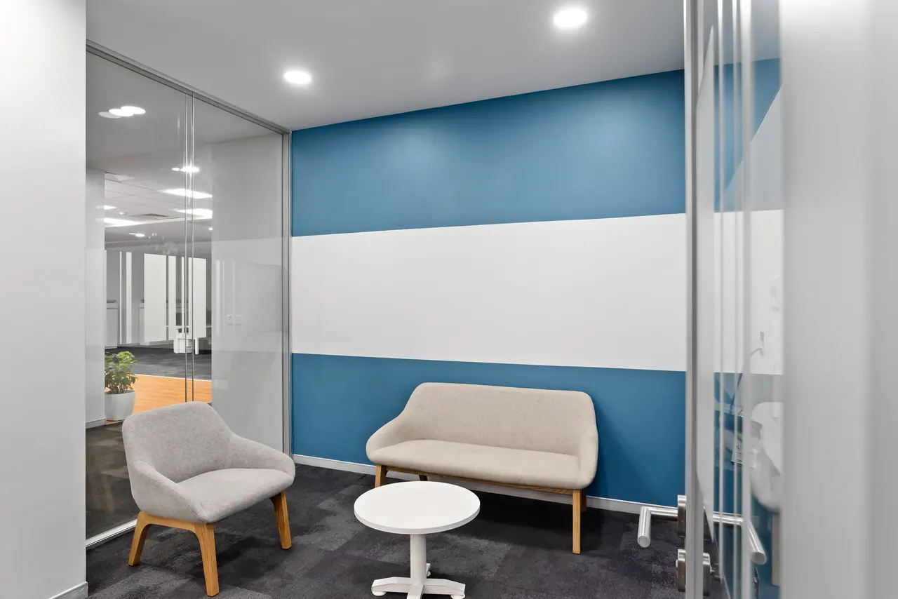 Small breakout room with a blue and white banded wall, a beige two-seater, a grey armchair and a round white table