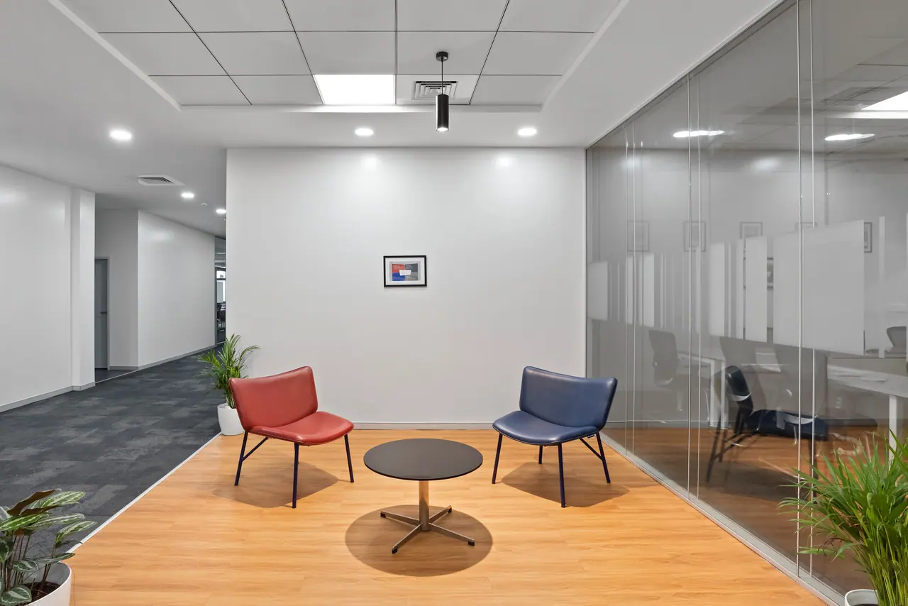 Lounge corner with red and blue leather chairs around a black side table on a wood floor beside frosted glass