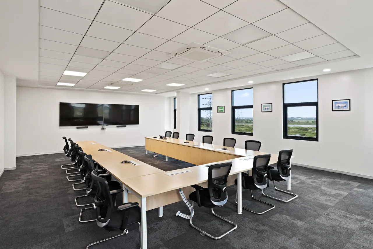 Conference room with a large U-shaped timber table, black mesh chairs, twin wall screens and black-framed windows