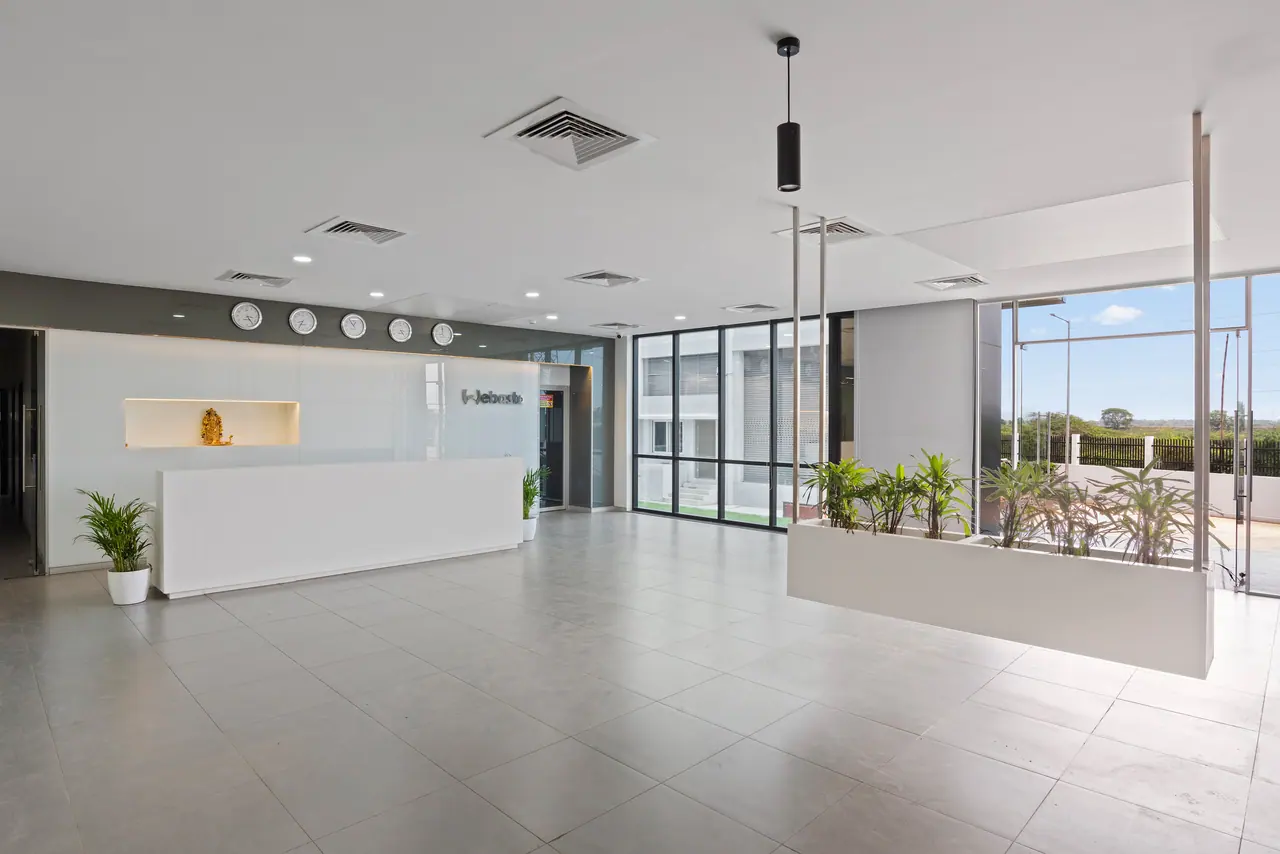 Reception lobby with a white desk, a row of wall clocks, a suspended planter and tall glazing onto the entrance