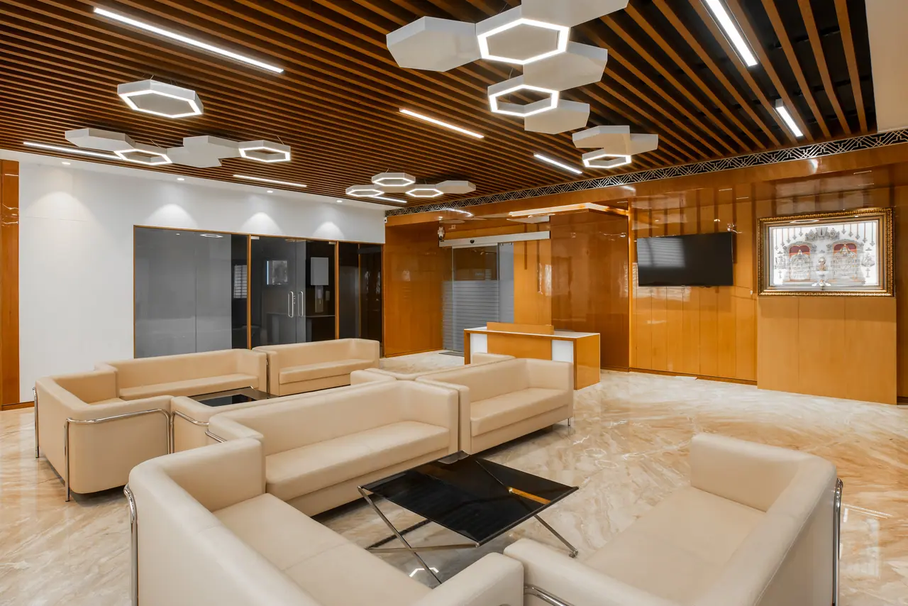 Lounge seating facing a reception counter, wall-mounted TV and gloss wood panelling under hexagonal light fixtures